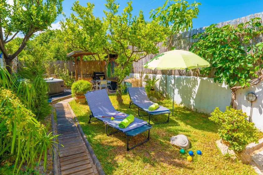 Un patio de jardín frondoso con asientos reclinables, una mesa sombreada y un sendero de madera.