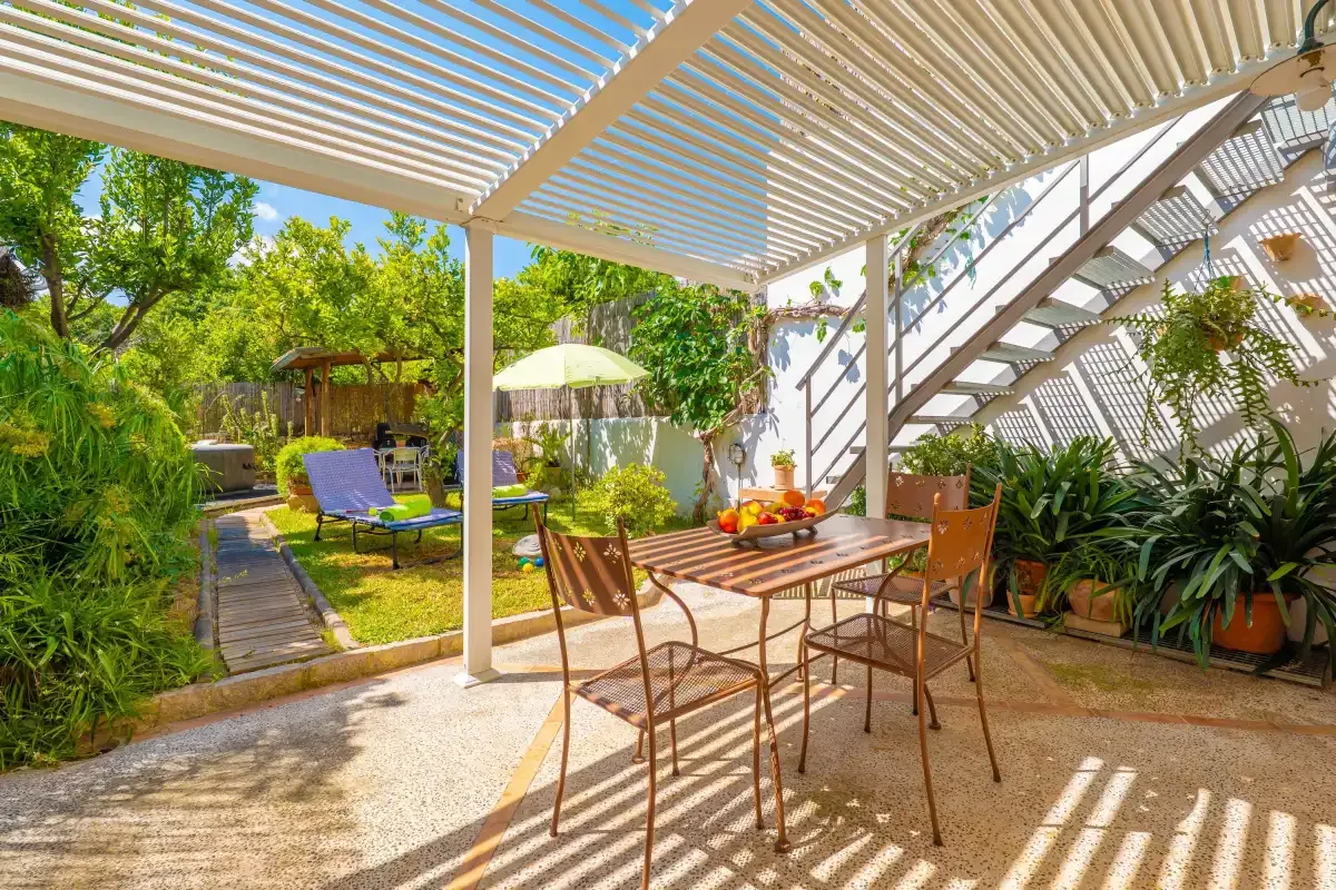 Una zona de comedor exterior a la sombra se abre a un jardín con asientos y vegetación.