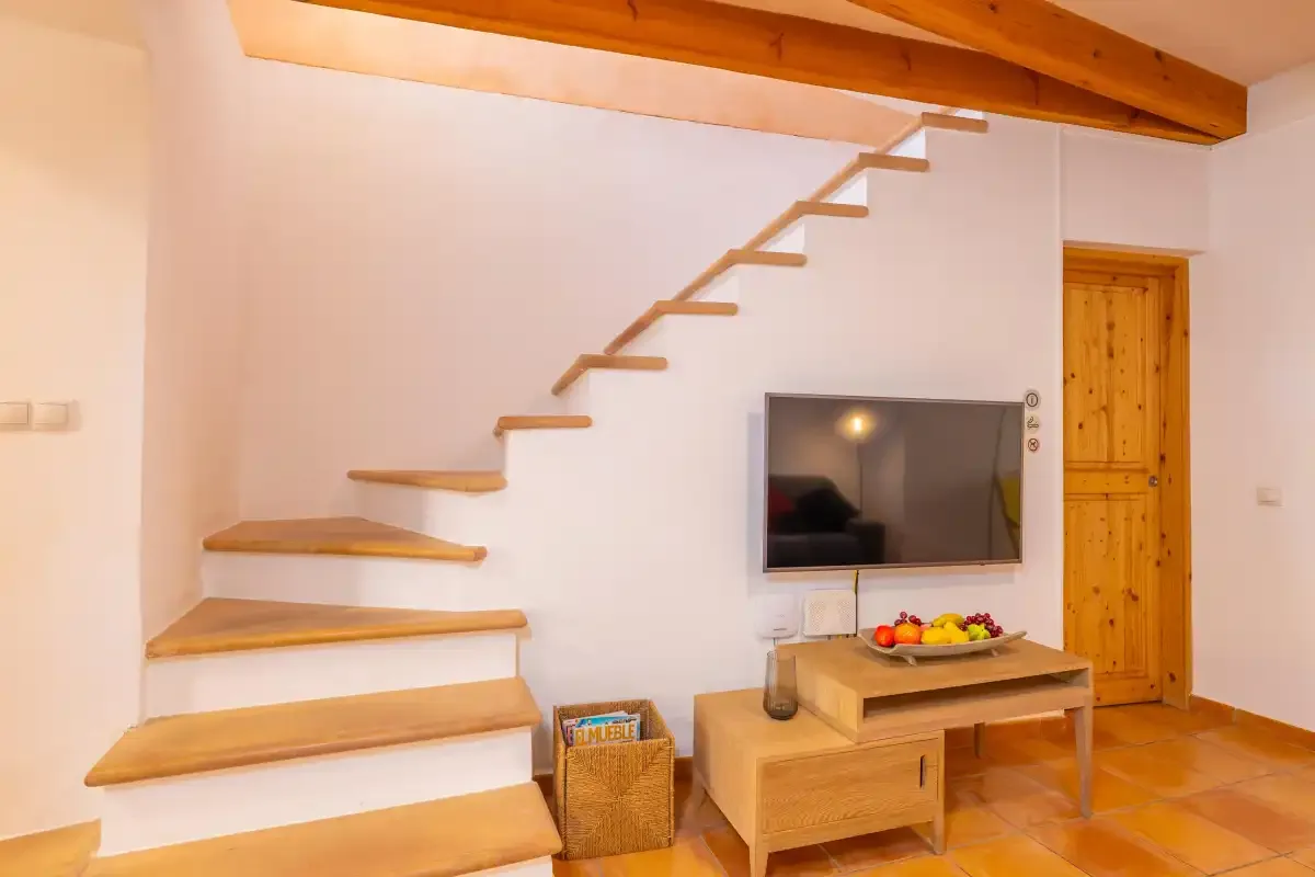 Una sala de estar con televisor, muebles de madera y una escalera.