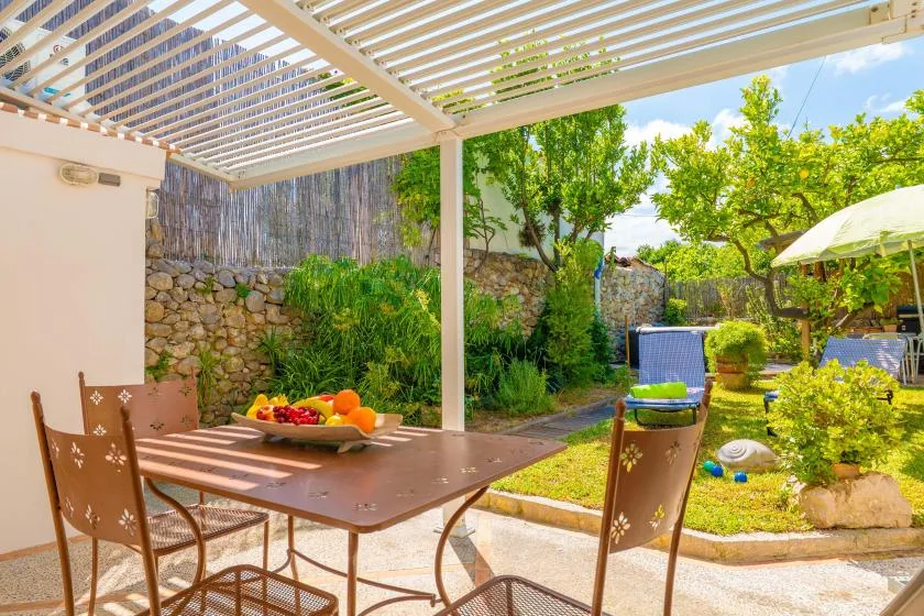 Una zona de comedor en un patio sombreado da a un jardín con una piscina pequeña.