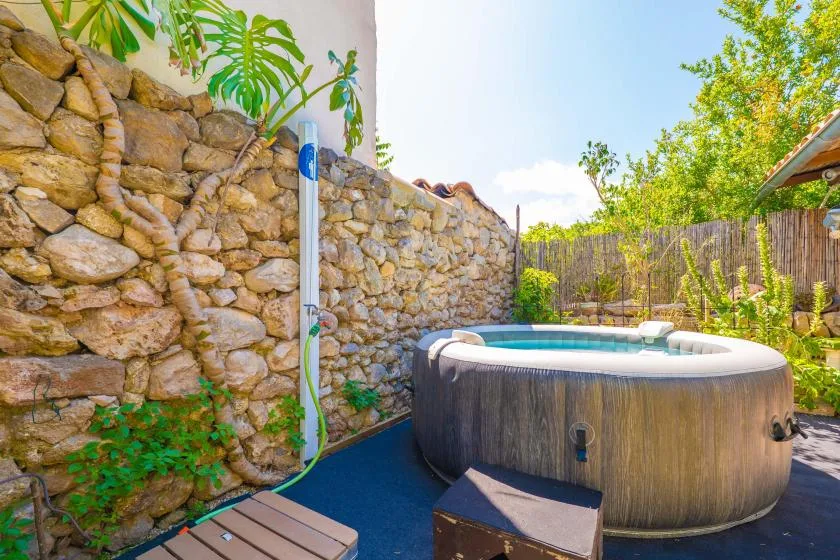 Un jacuzzi al aire libre está junto a un muro de piedra y plantas.