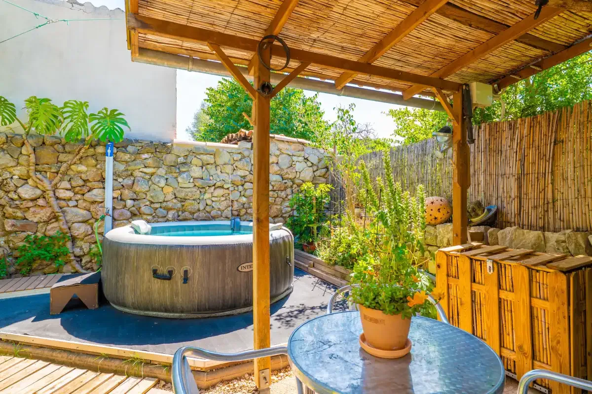 Un jacuzzi exterior cubierto está junto a un muro de piedra y plantas.