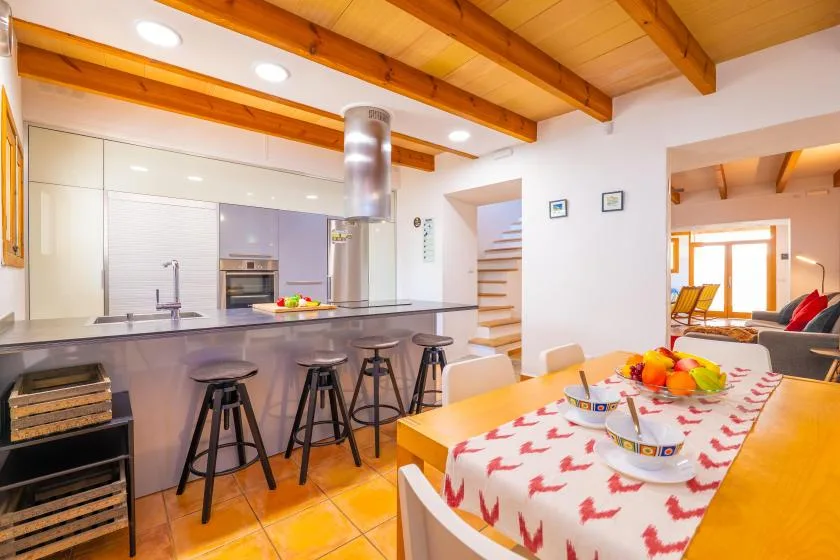 Cocina y comedor de planta abierta, con barra de desayuno y vigas de madera a la vista.