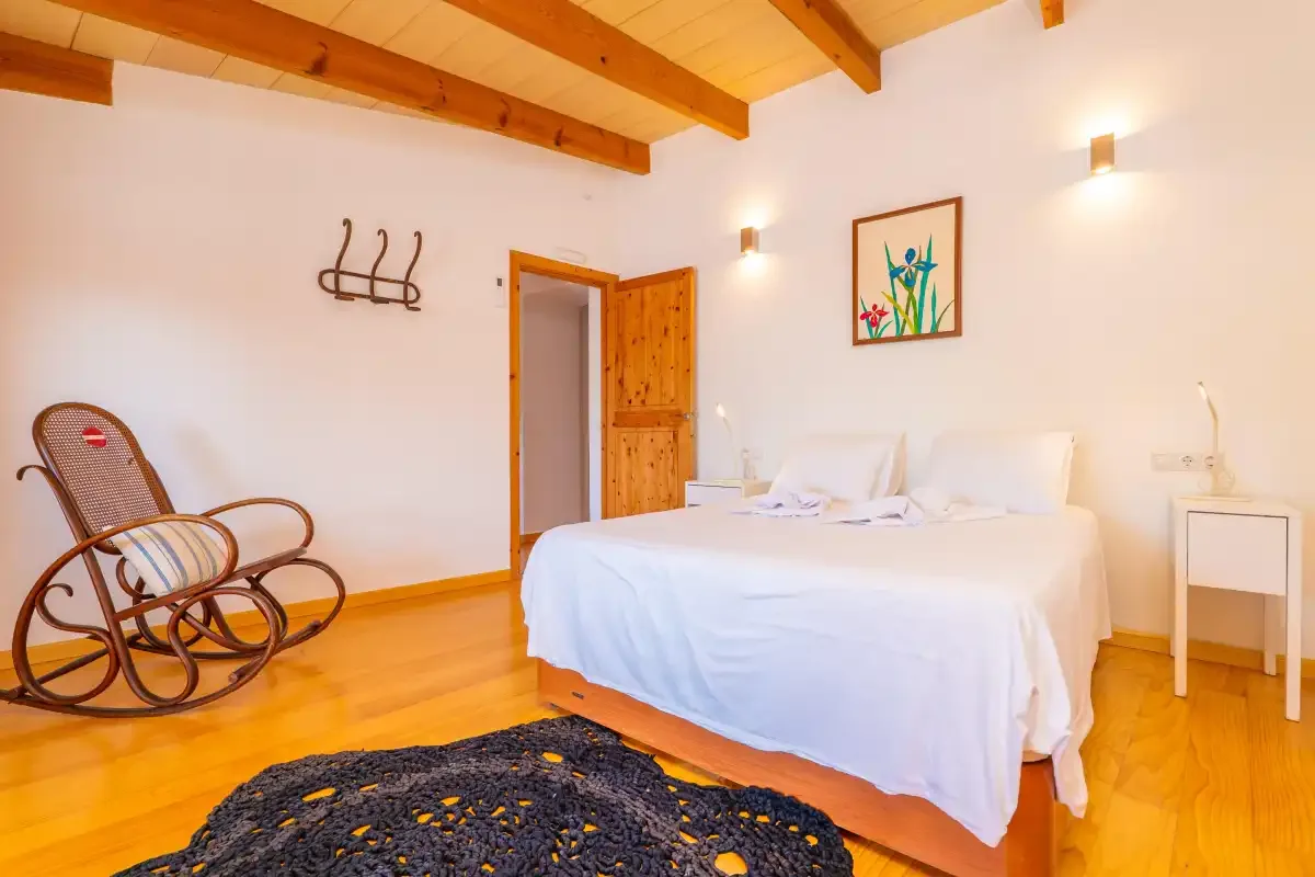 Un dormitorio con una cama blanca, vigas de madera en el techo y una mecedora.
