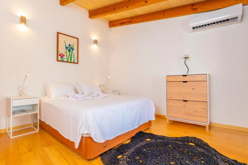Un dormitorio luminoso con una cama, vigas de madera en el techo y una cómoda.