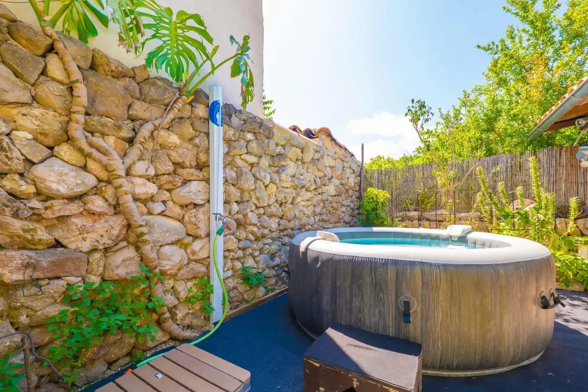 Un patio exterior cuenta con una bañera de hidromasaje redonda junto a un muro de piedra.