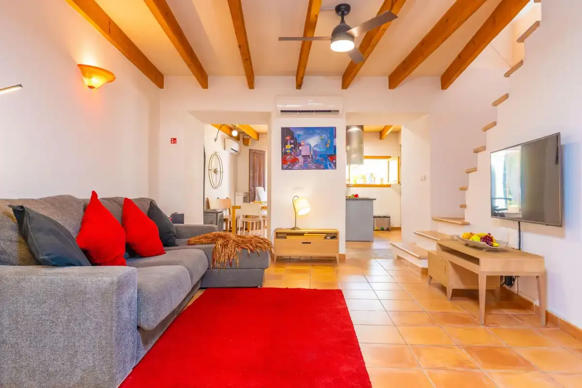 Sala de estar con asientos, una alfombra roja y una cocina abierta.