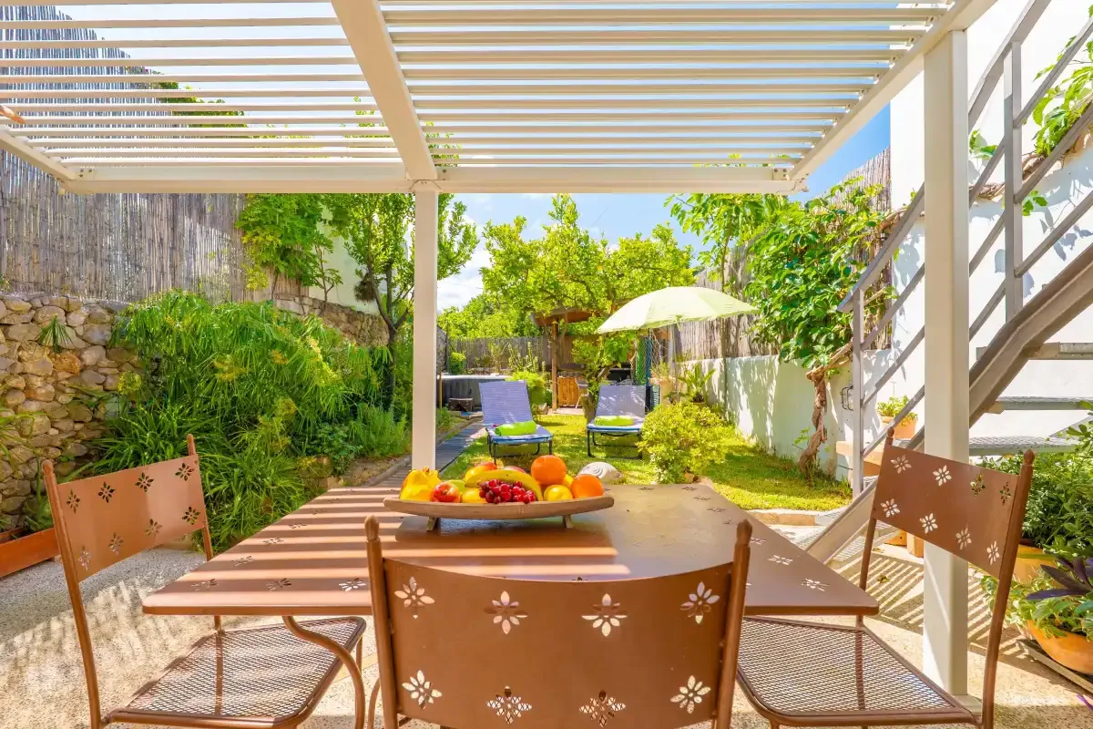 Una zona de comedor en un patio sombreado, con asientos al aire libre y un jardín al fondo.
