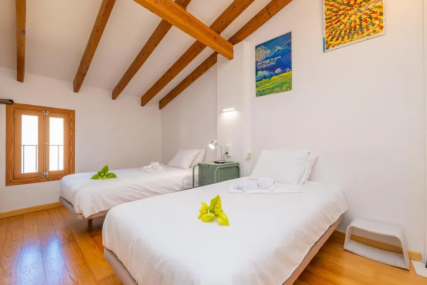 Un dormitorio luminoso con dos camas, suelo de madera y vigas vistas en el techo.