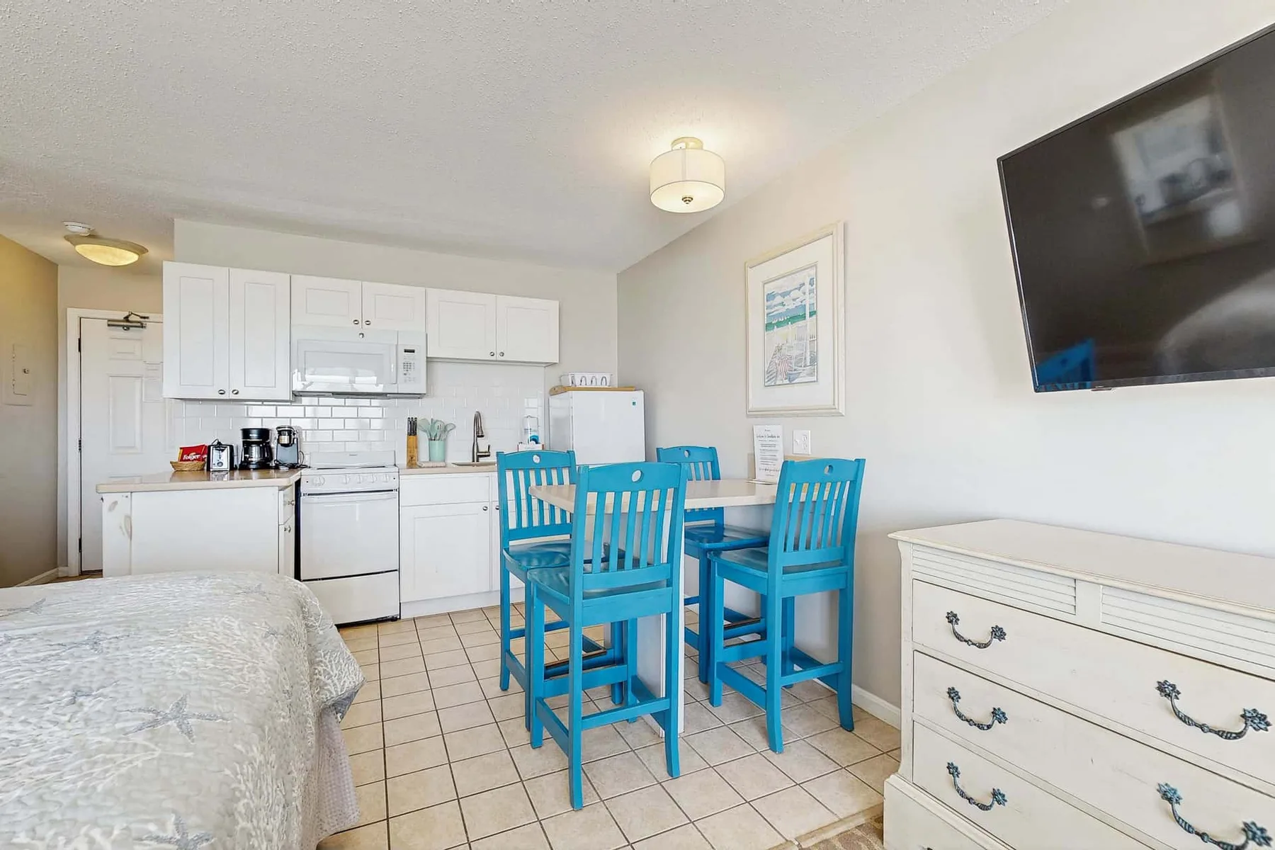 A bedroom and kitchen share a bright open room with a blue dining table.