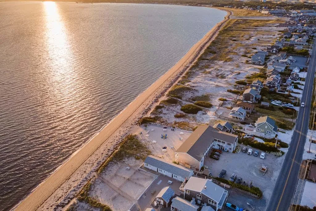 Vista aérea de un vecindario costero junto a una playa de arena y aguas tranquilas.