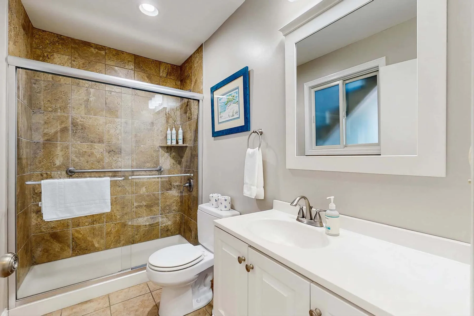 Un baño con ducha revestida de azulejos, inodoro y tocador blanco.