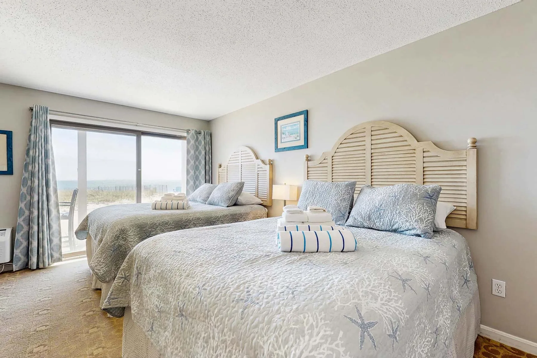 Un dormitorio con dos camas, ropa de cama estampada y una ventana grande.