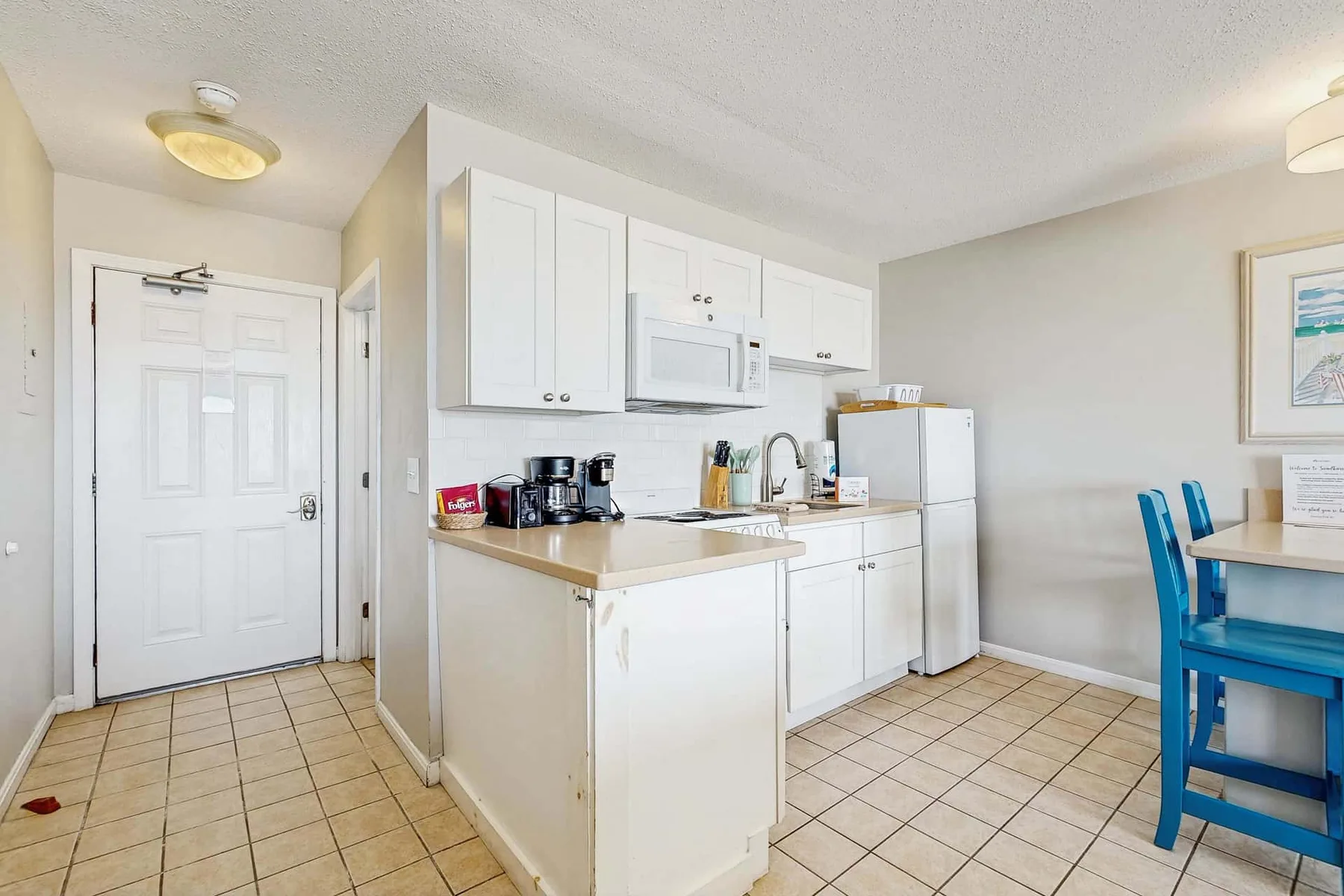 Una cocina pequeña con gabinetes blancos, un refrigerador y una mesa de comedor.