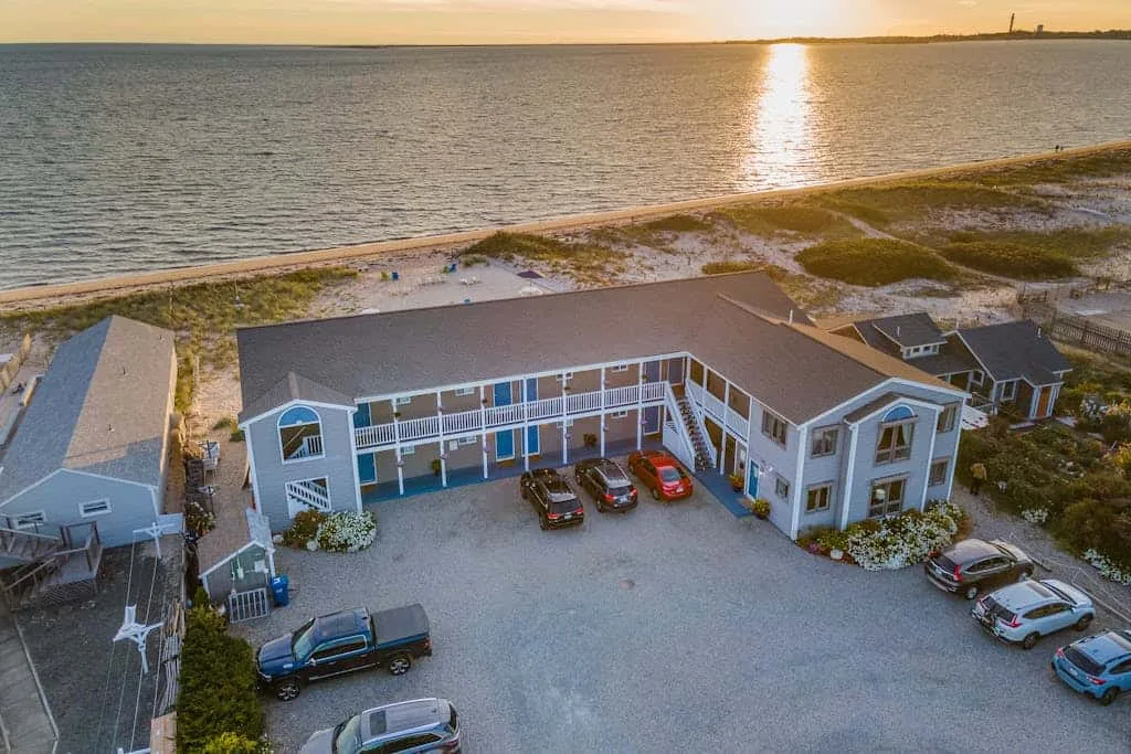Aerial view of a waterfront building beside a broad parking area at sunset.