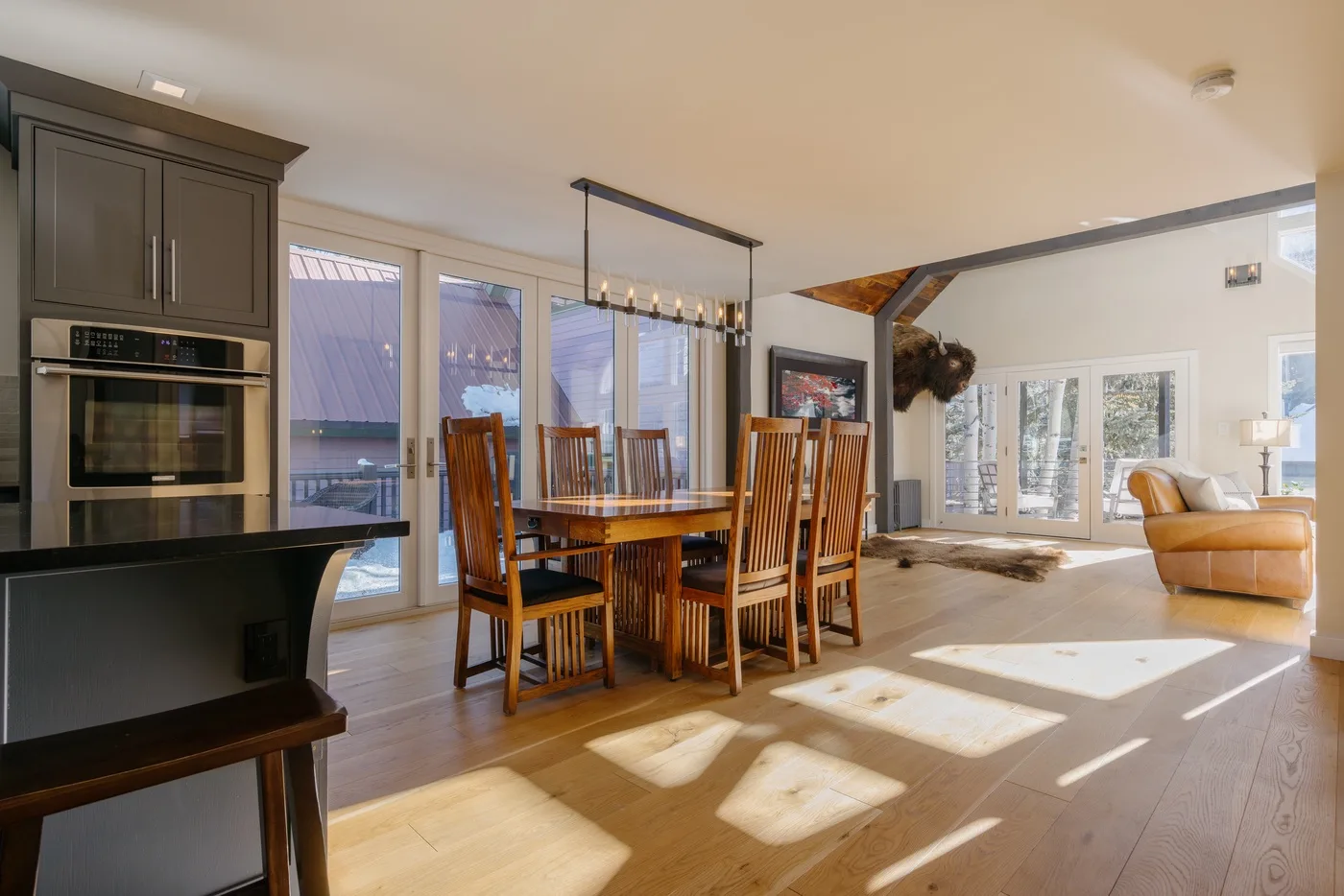 Una zona abierta de comedor y sala de estar cuenta con una mesa de madera y grandes ventanas.