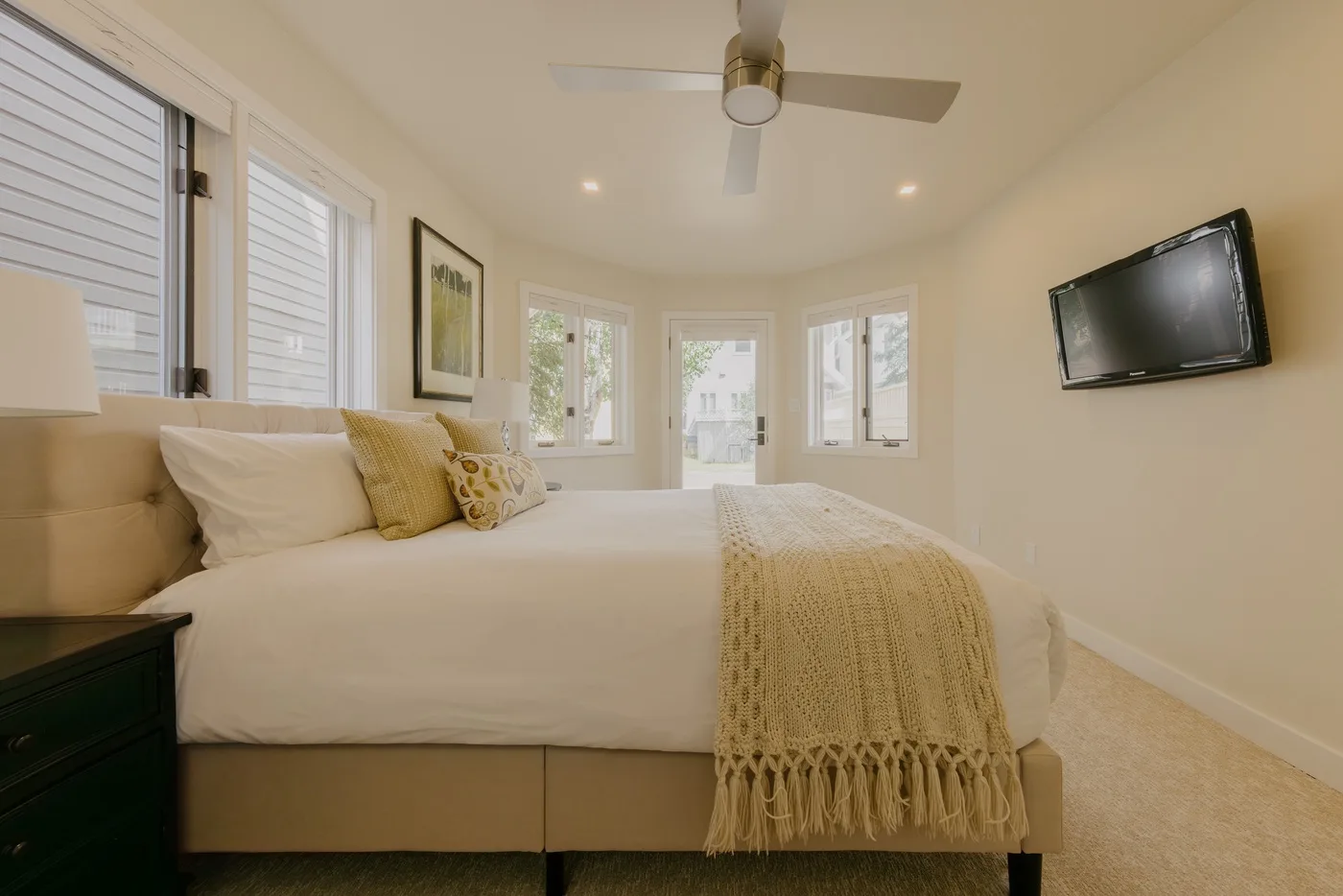 Un dormitorio luminoso con una cama bien hecha y un televisor en la pared.