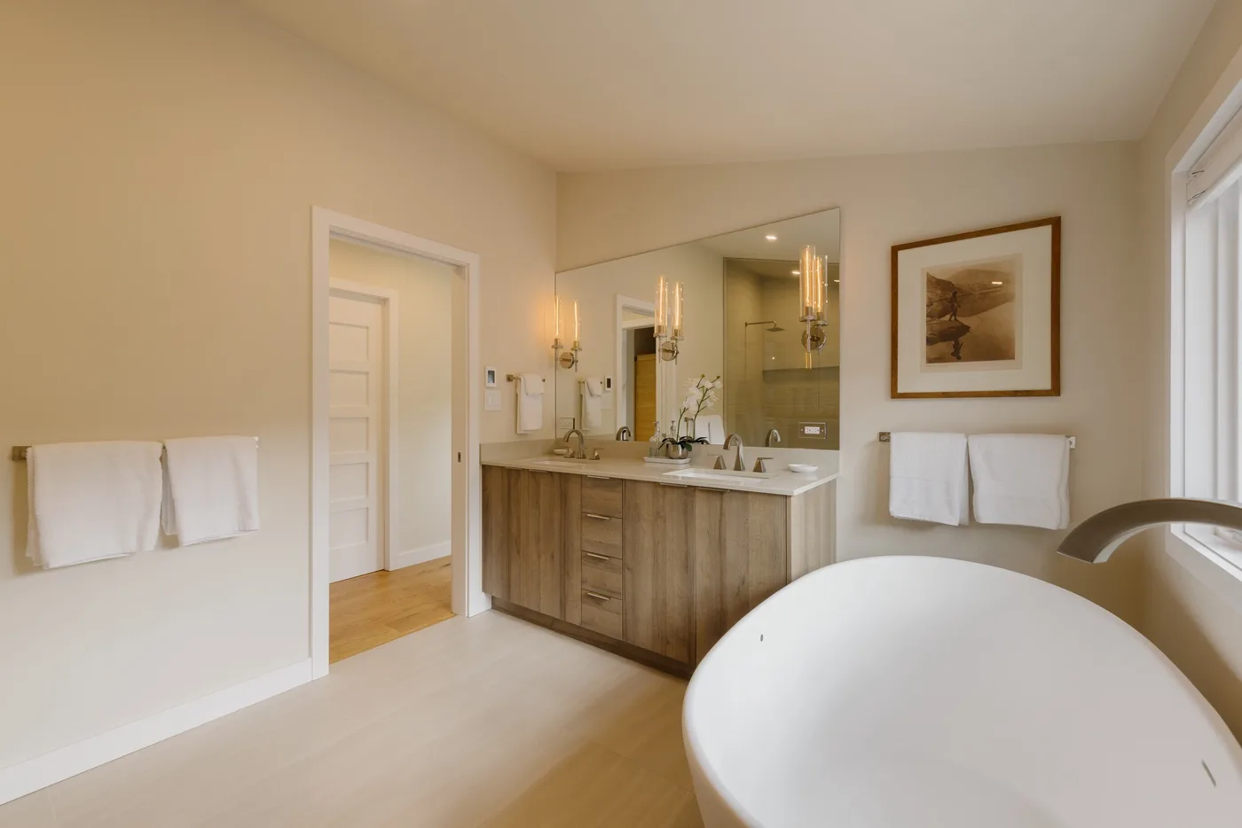 Un baño luminoso con tocador de madera, espejo grande y bañera exenta.