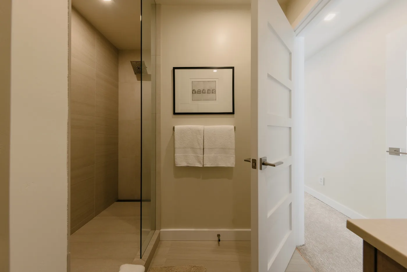 Un baño con una ducha de vidrio, toallas y un cuadro enmarcado.