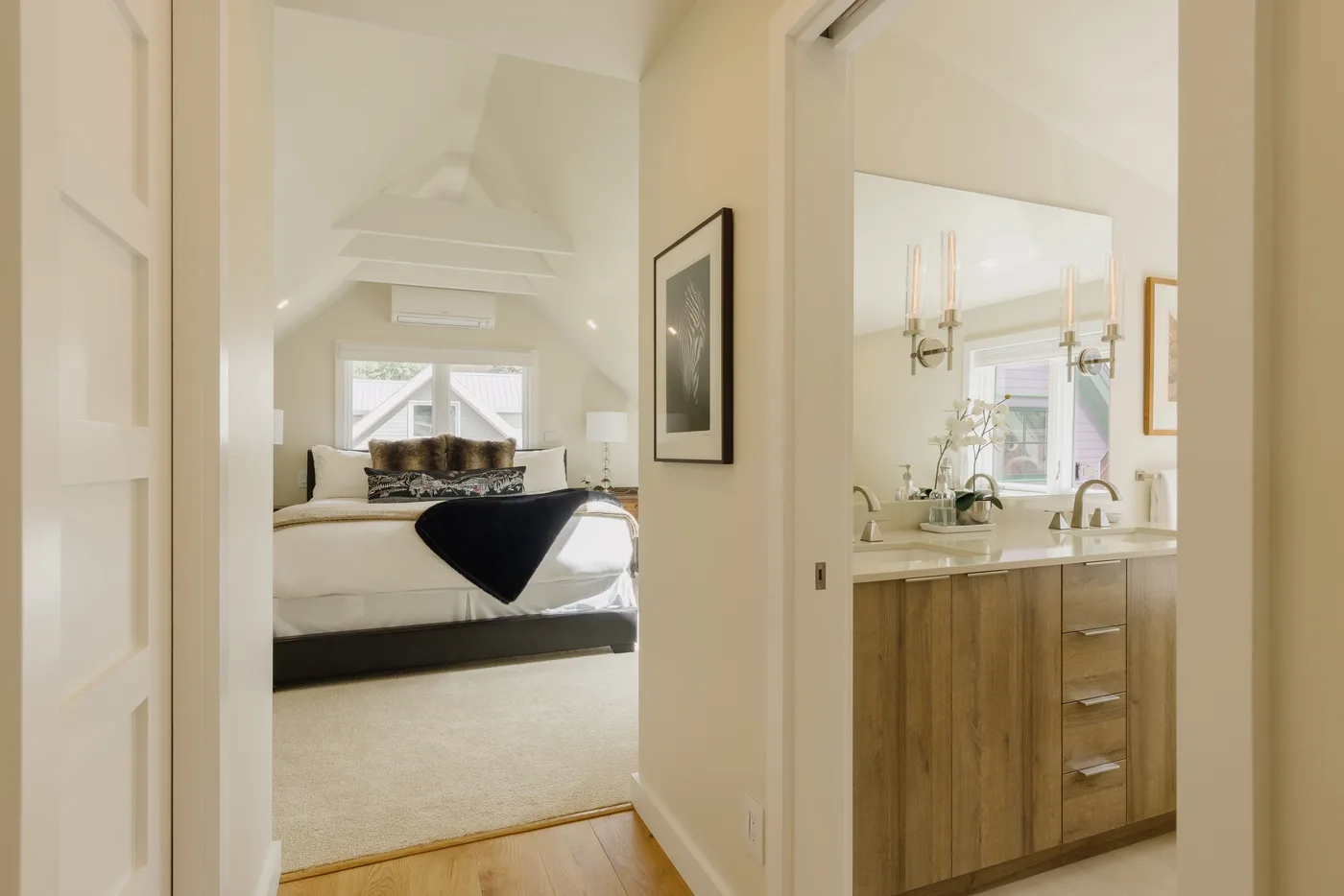 Se ve un dormitorio con la cama tendida junto a un tocador de baño abierto.