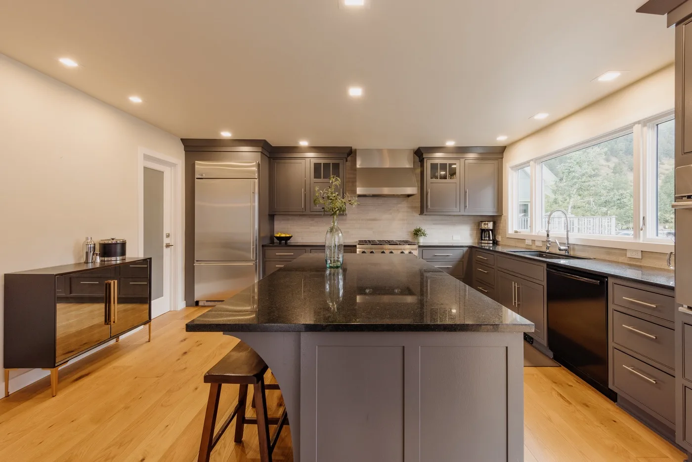 Una cocina moderna con una isla central grande, armarios oscuros y ventanas amplias.