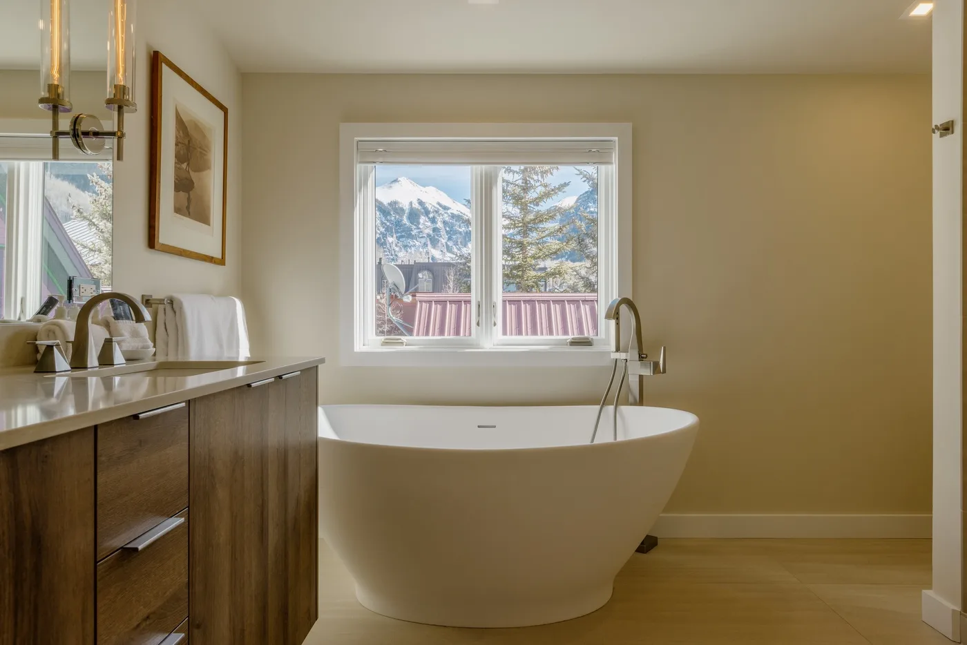 Un baño con una bañera exenta bajo una ventana con vistas a árboles y montañas.
