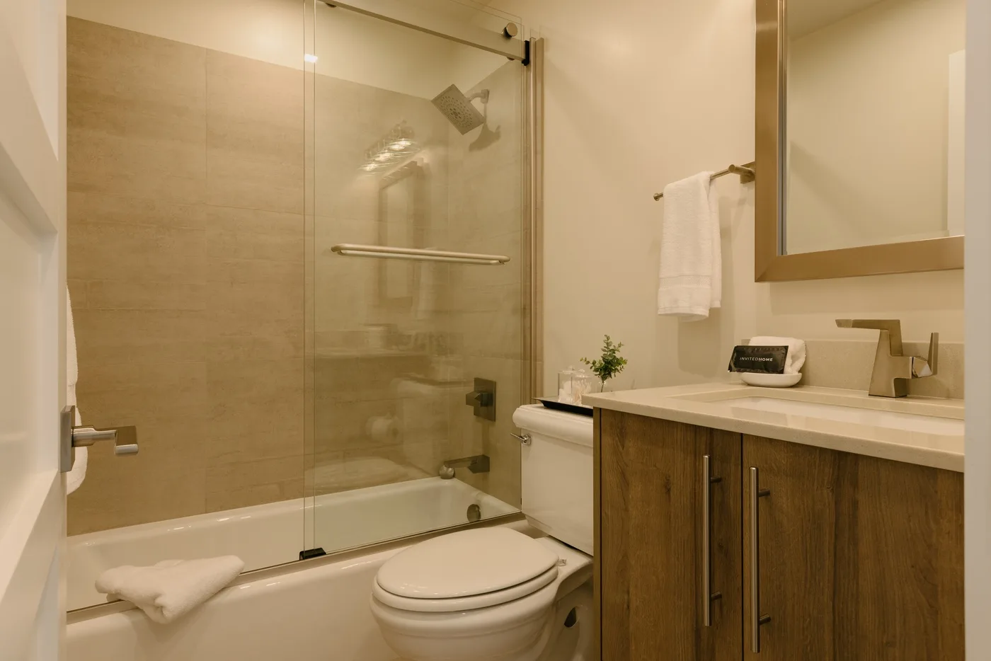Un baño con ducha de vidrio, inodoro y tocador con frente de madera.