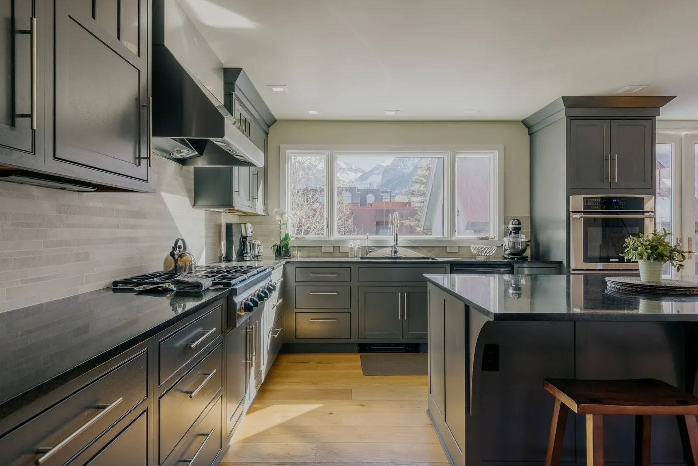 Una cocina moderna con gabinetes oscuros, una isla central y ventanas con vista al exterior.