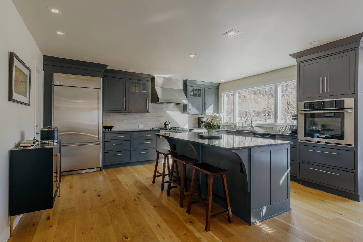 Una cocina moderna con gabinetes oscuros, una isla central y grandes ventanas.
