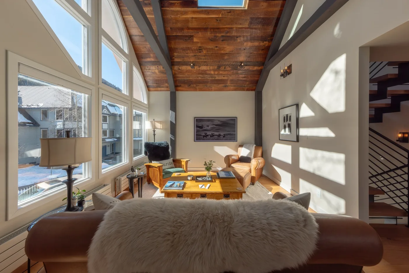 Una sala luminosa con ventanas altas, vigas de madera y asientos alrededor de una mesa de centro.