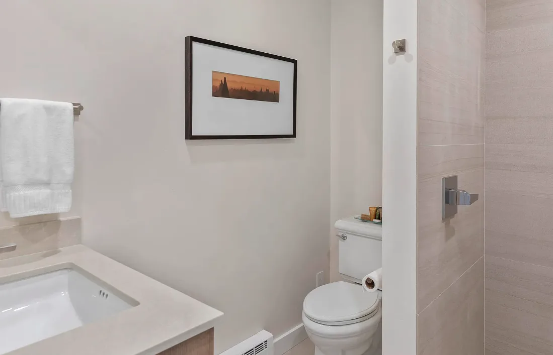 Un baño con lavabo, inodoro y una obra enmarcada en la pared.