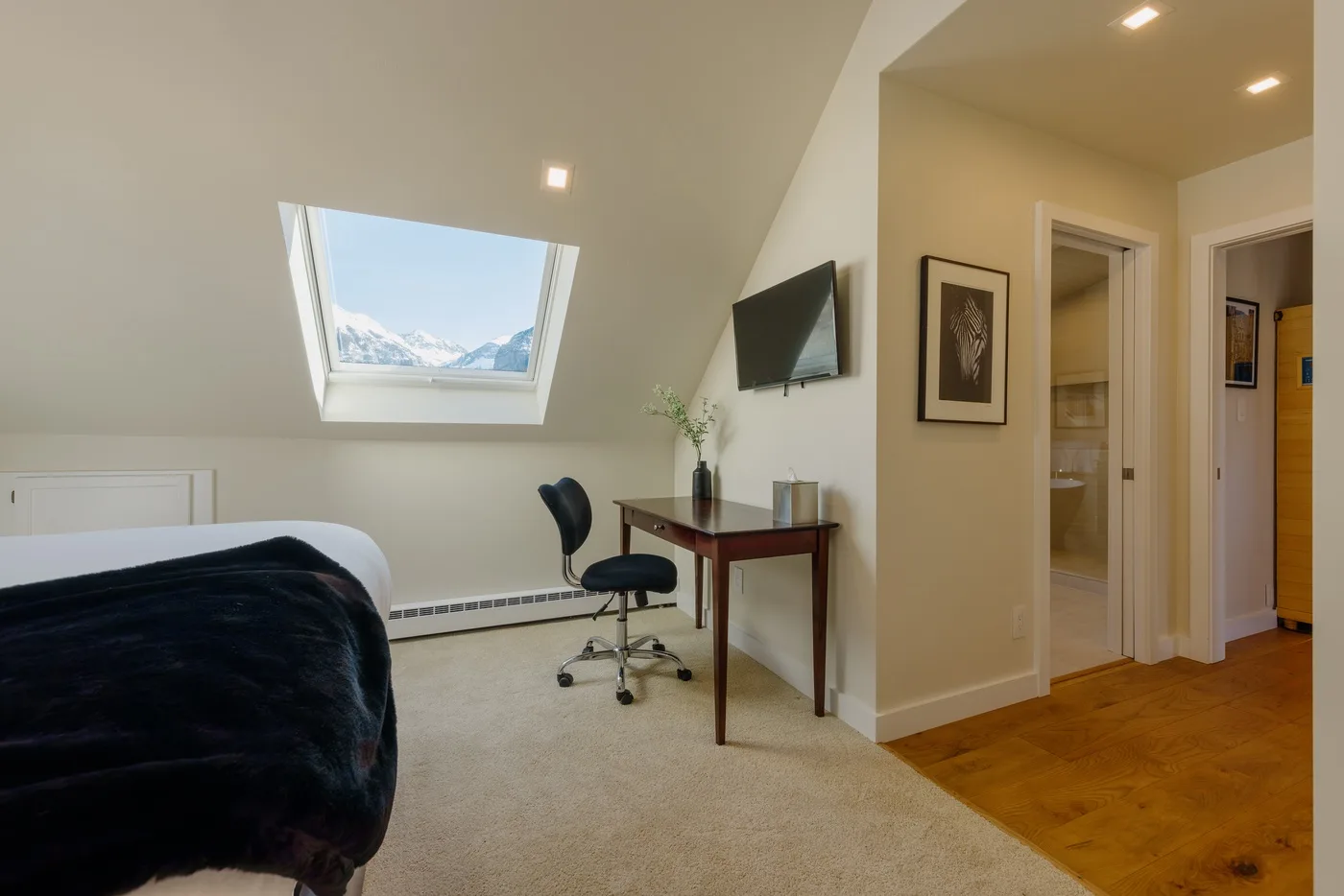 Un dormitorio con escritorio y silla bajo un techo inclinado y una claraboya.