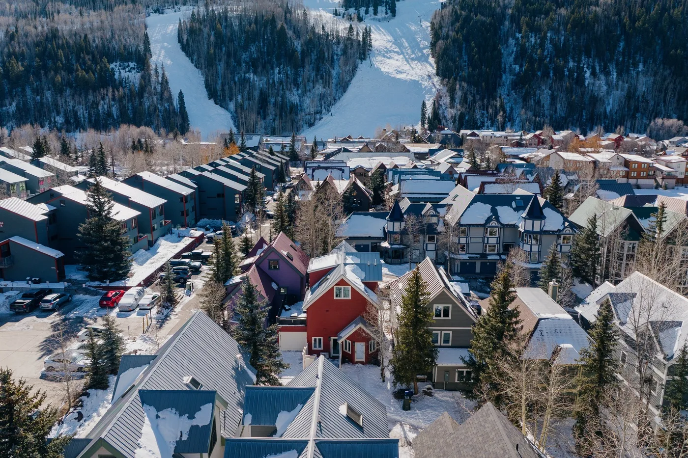 Vista aérea de un pueblo de montaña nevado, rodeado de laderas boscosas para esquiar.