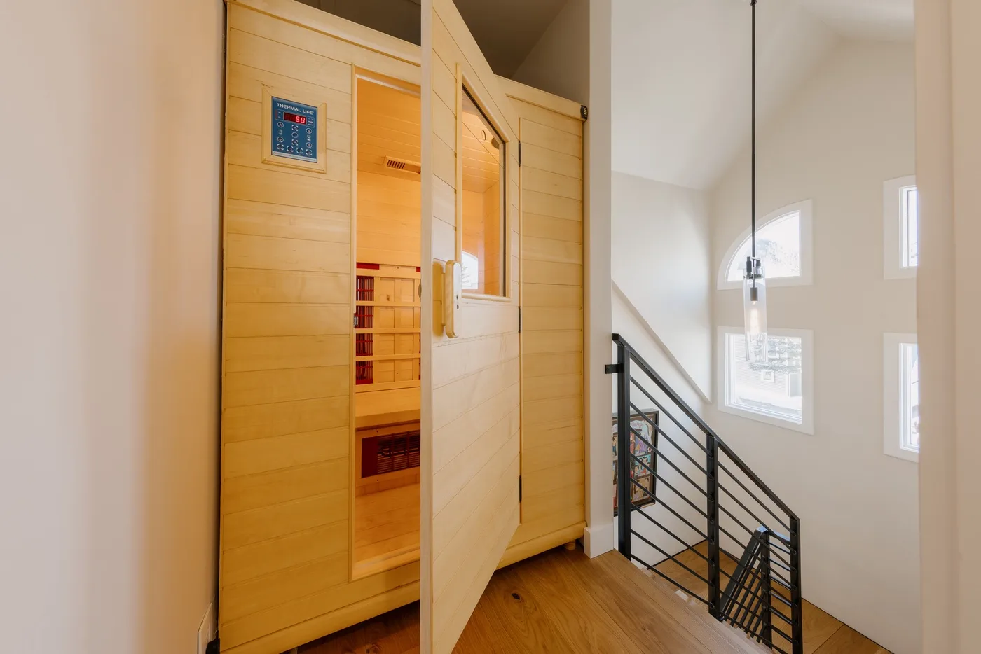 Una sauna de madera está junto a una escalera en un interior luminoso.