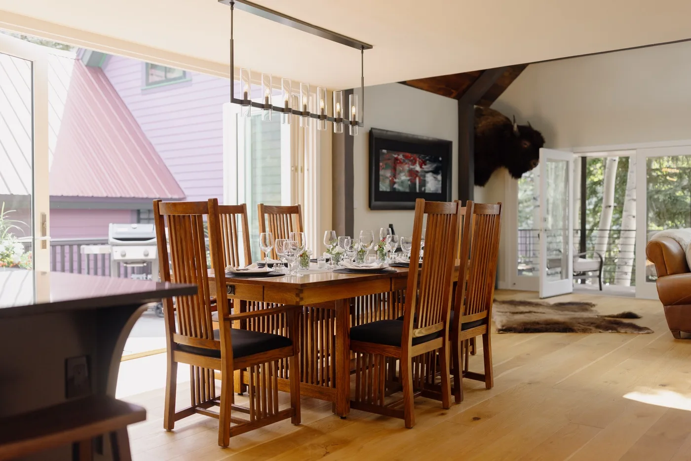 Un comedor con una mesa de madera y sillas altas junto a grandes ventanas.