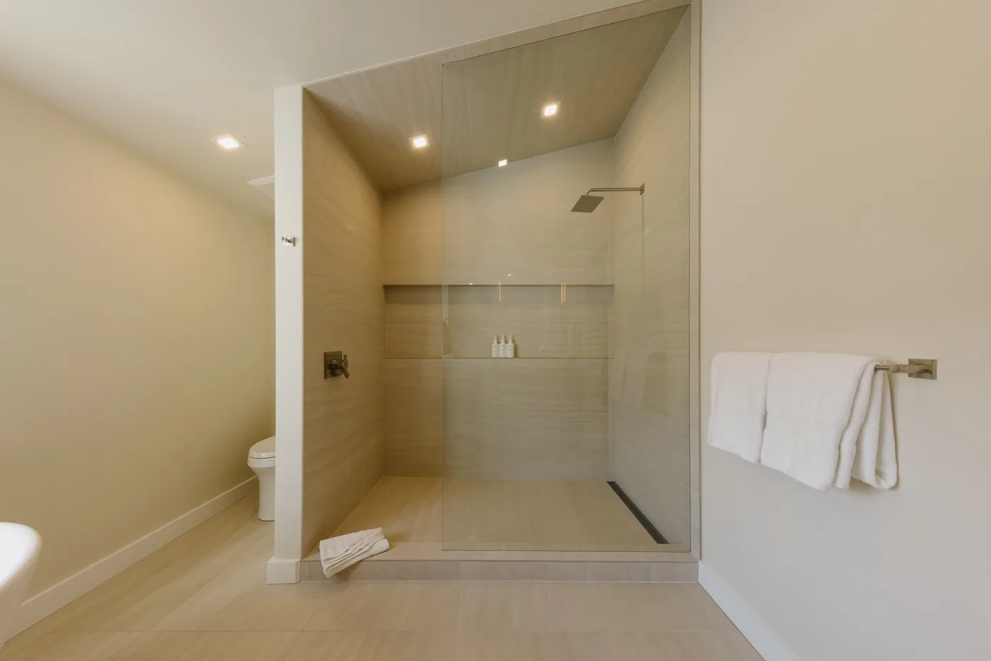 Un baño con una ducha con frente de vidrio y azulejos claros.