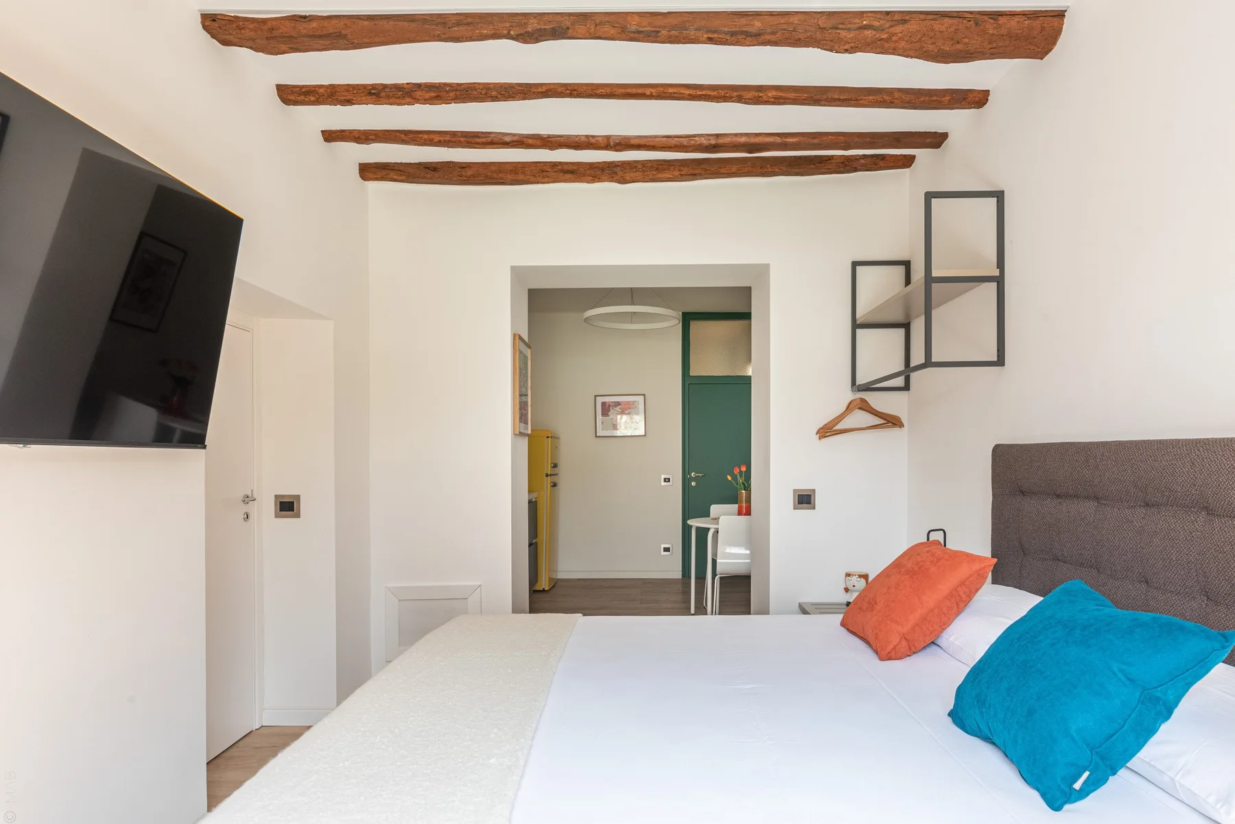 A bedroom with a bed, colorful pillows, and exposed ceiling beams.