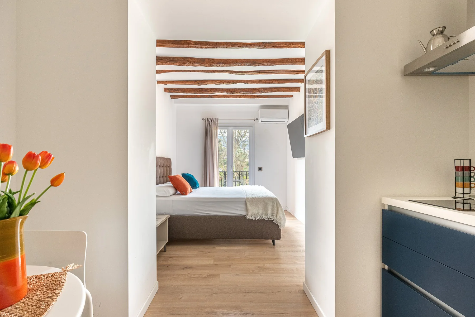 A bedroom with a bed beneath exposed ceiling beams and doors opening to a balcony.