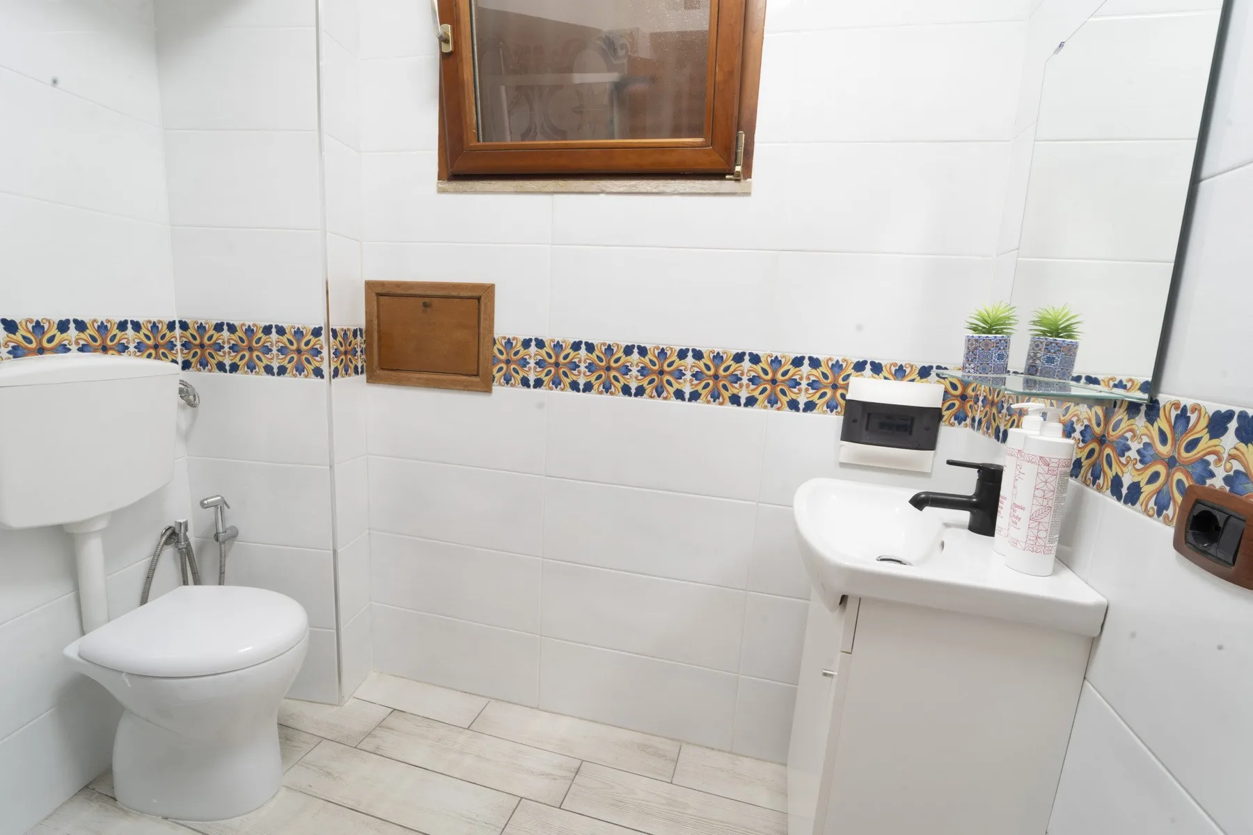 A tiled bathroom with a toilet and a sink beneath a small window.