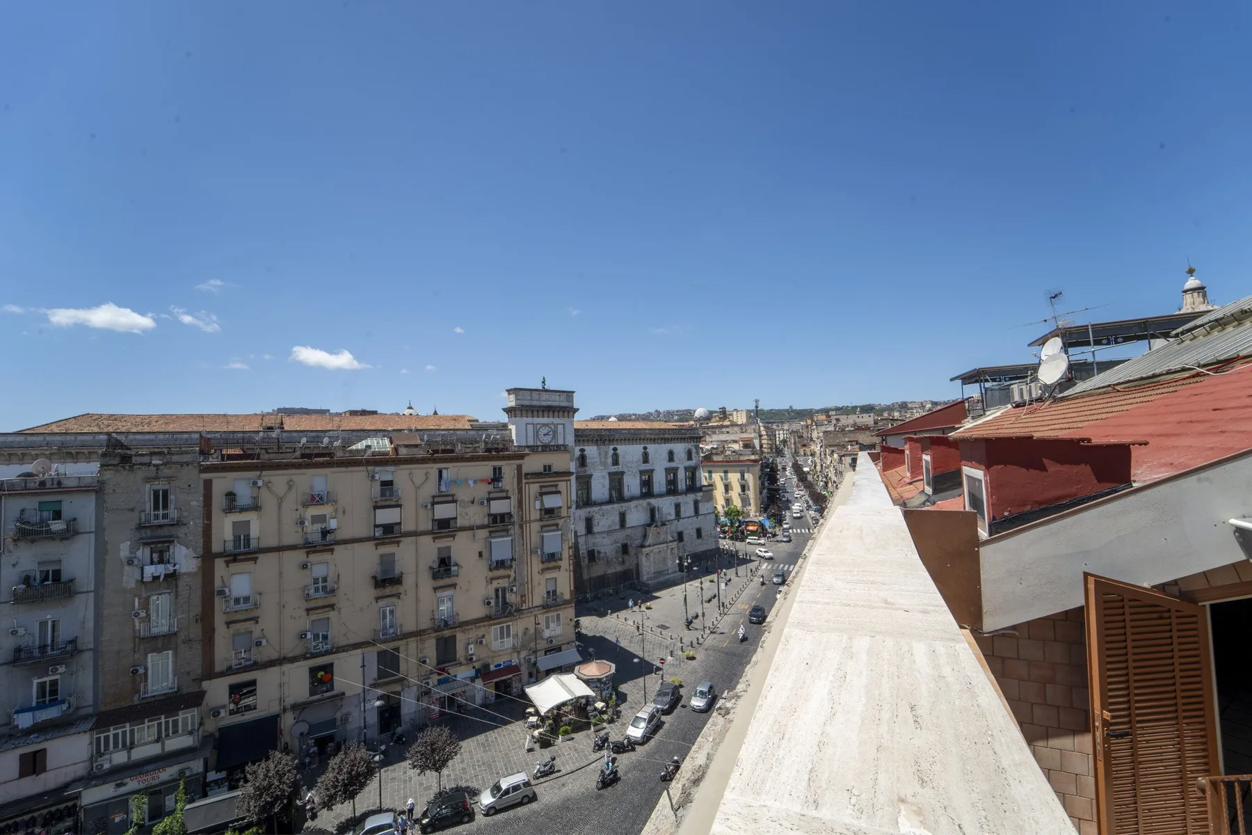 Rooftop view over a city street lined with buildings beneath a clear blue sky.