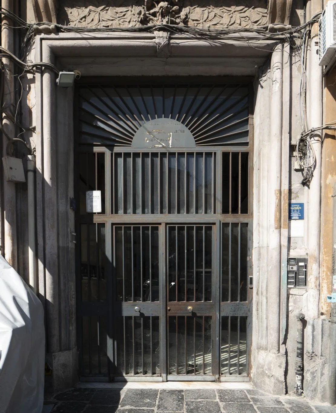 A barred entrance gate sits within a stone doorway on a narrow street.