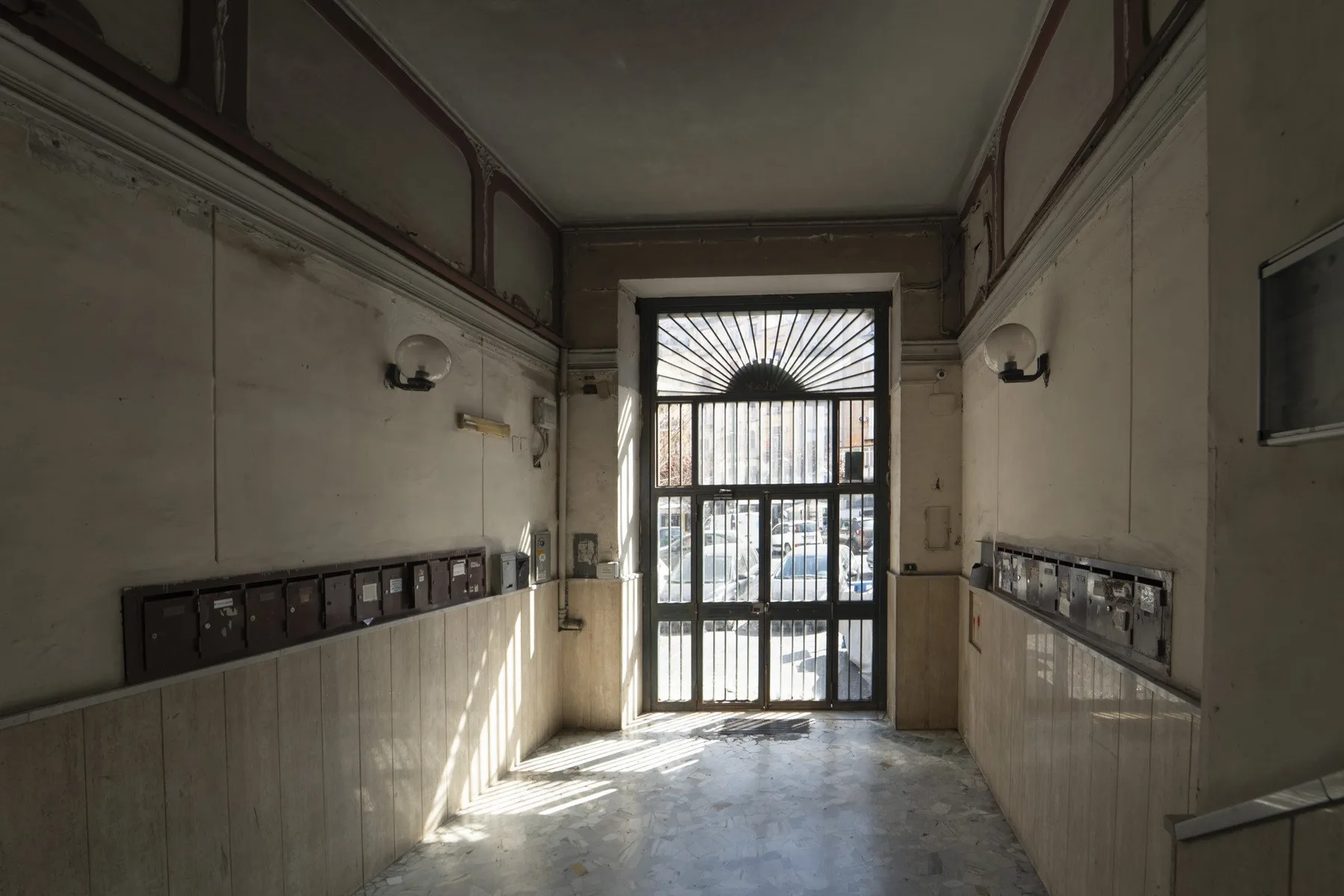 An interior hallway with a barred glass entrance and wall-mounted mailboxes.