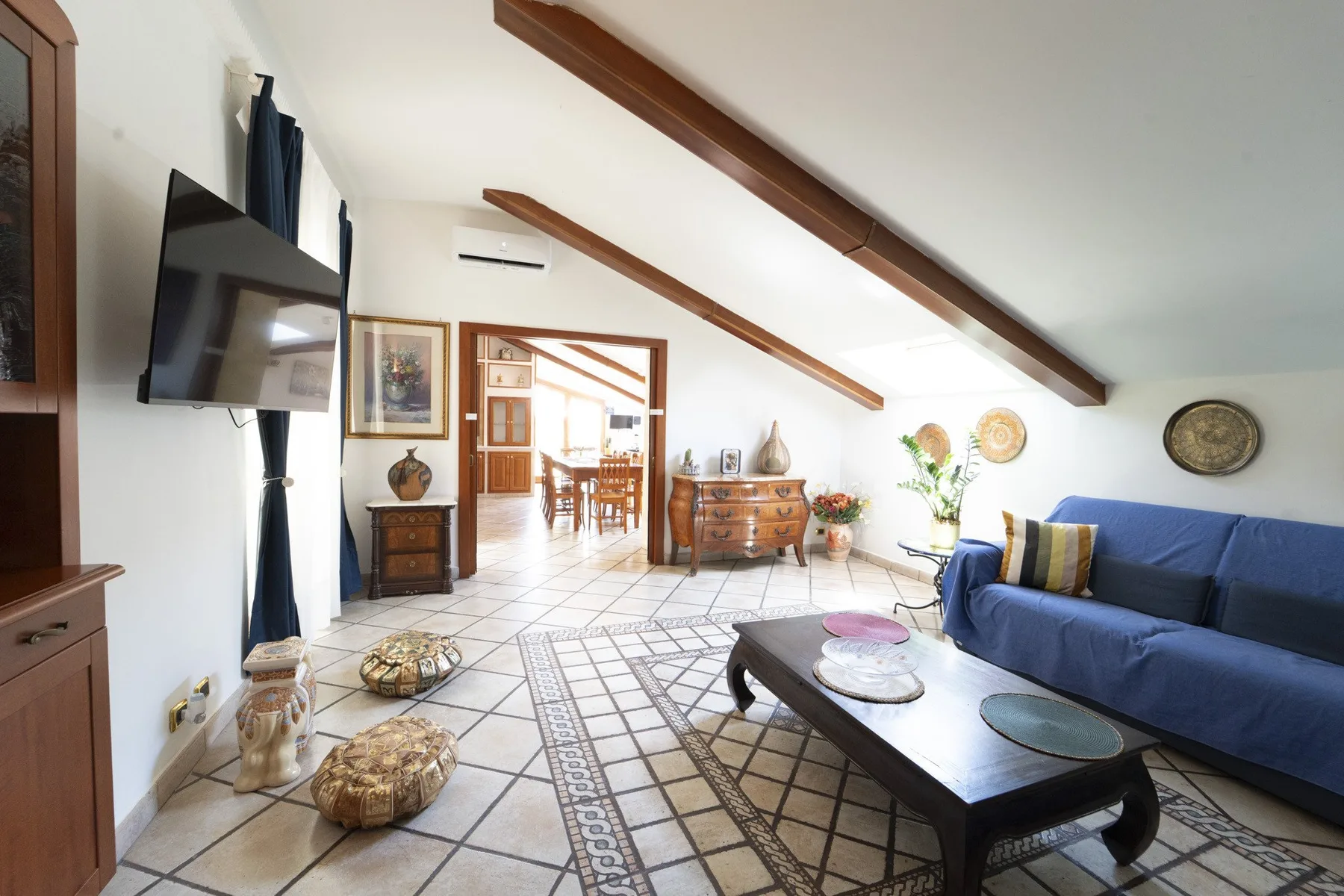 A bright living room with blue seating, a coffee table, and exposed ceiling beams.