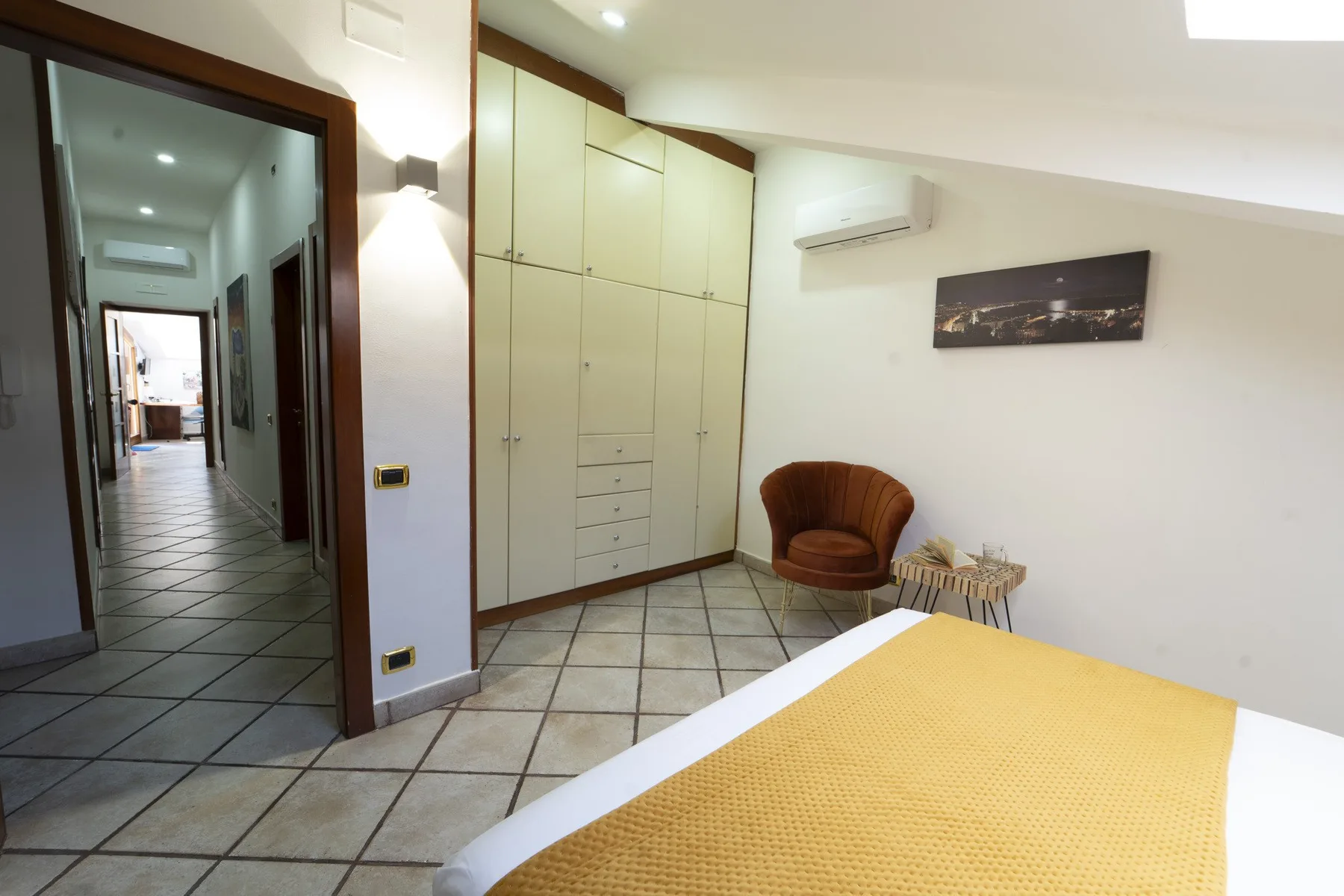 A bedroom with a yellow bedspread, built-in cabinets, and a small seating area.