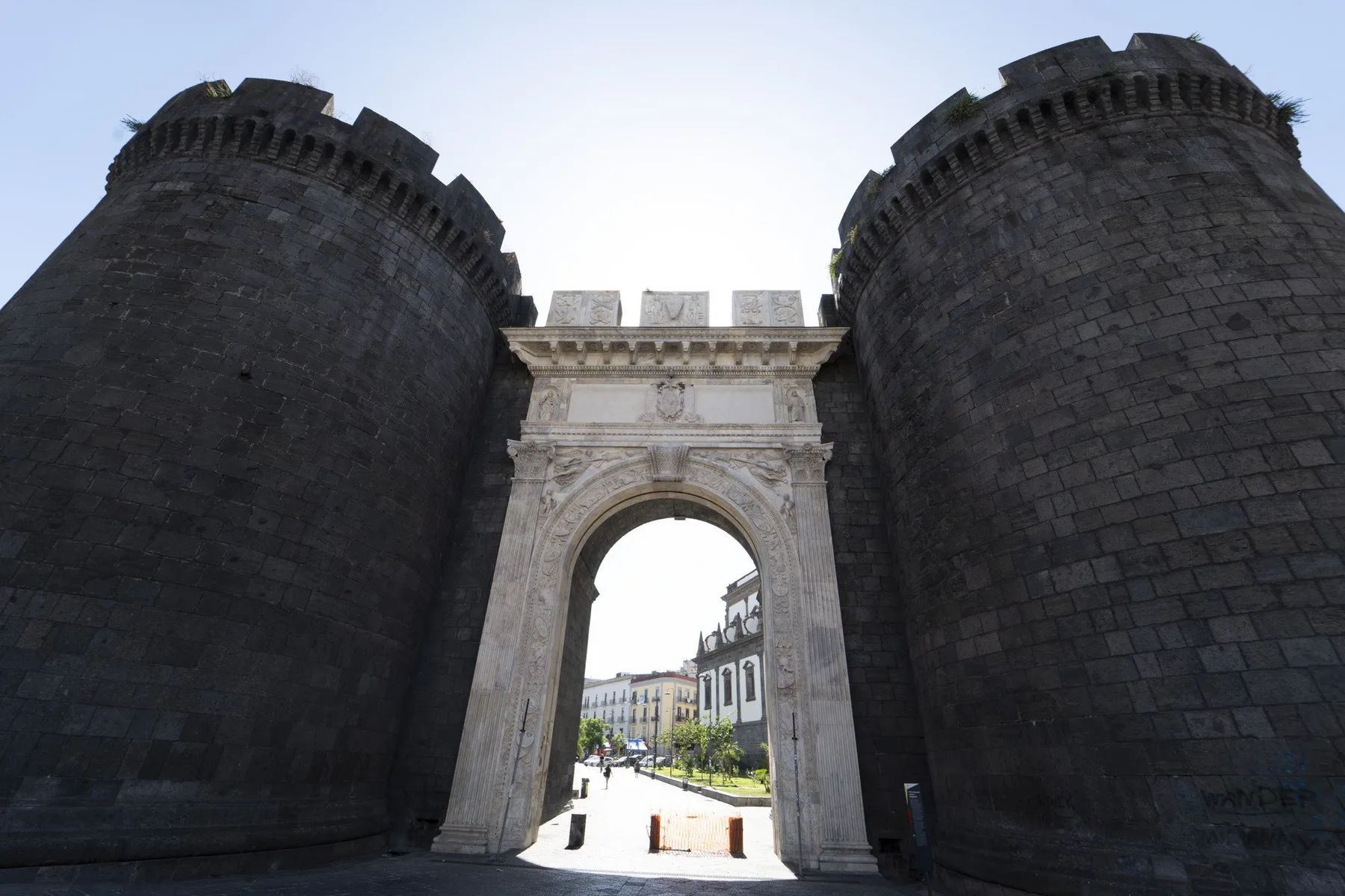 A stone gateway stands between two dark round towers, opening onto a city street.