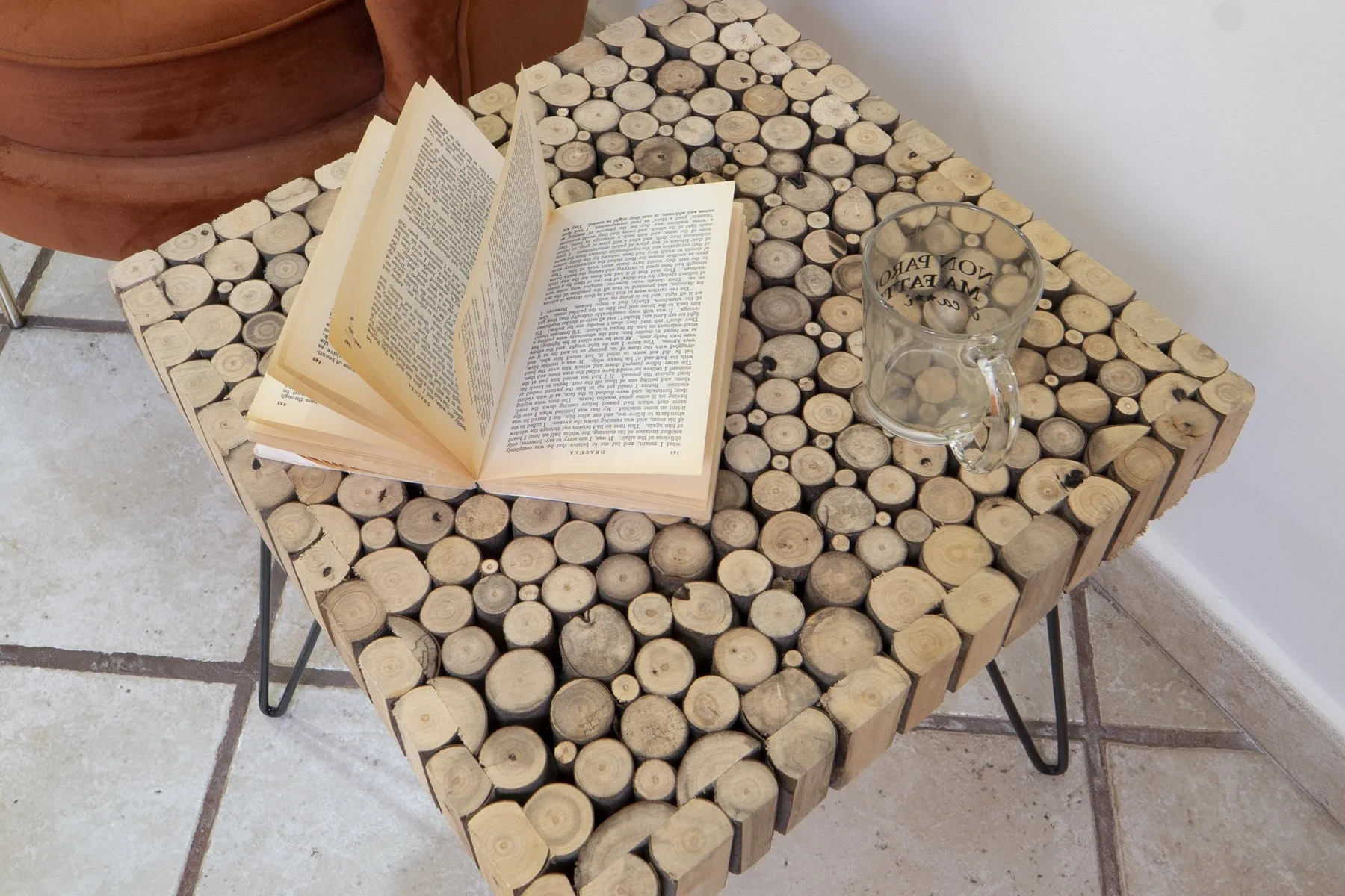 A small table made from wood rounds holds an open book and a glass.