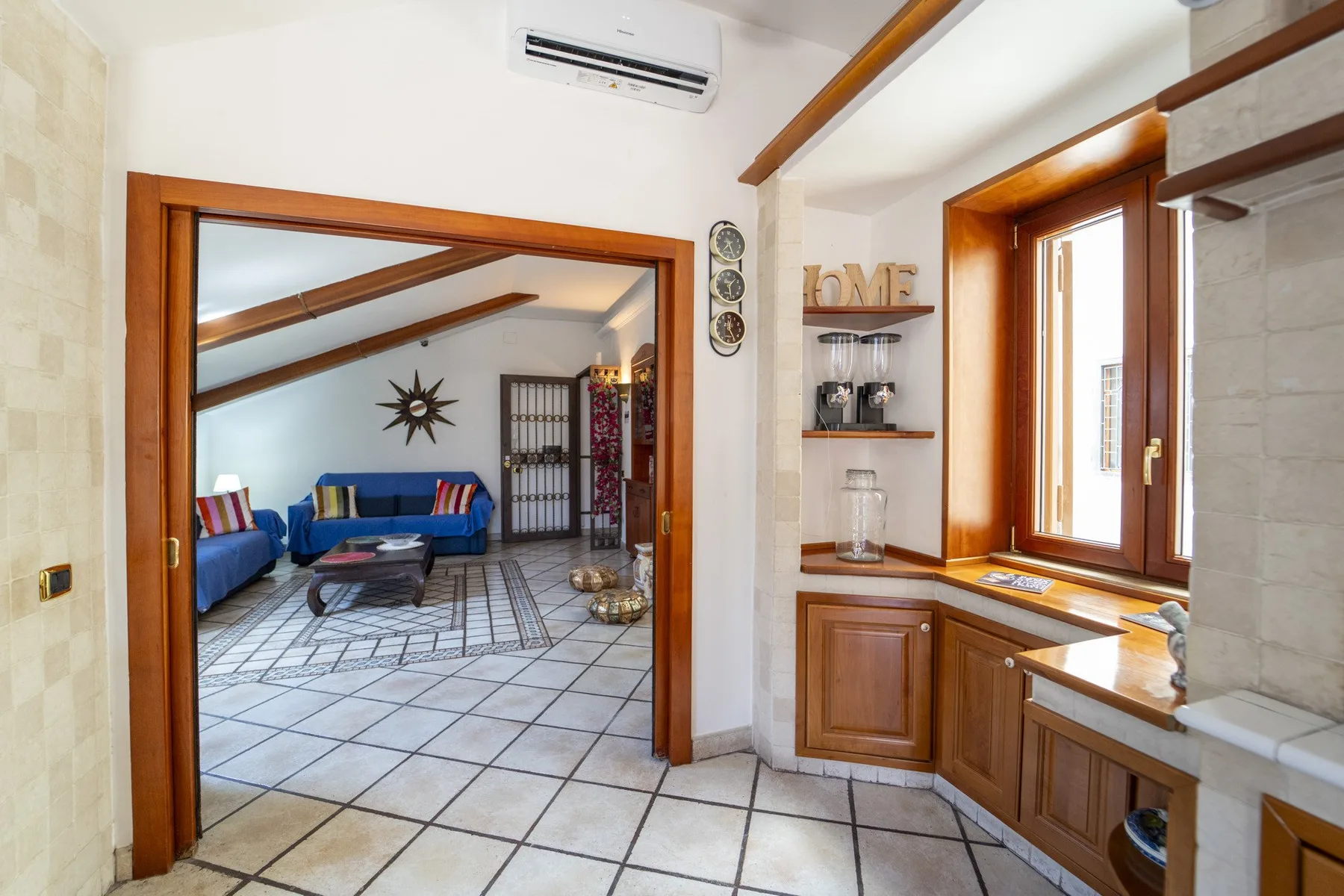 A tiled kitchen opens onto a living area with blue seating.