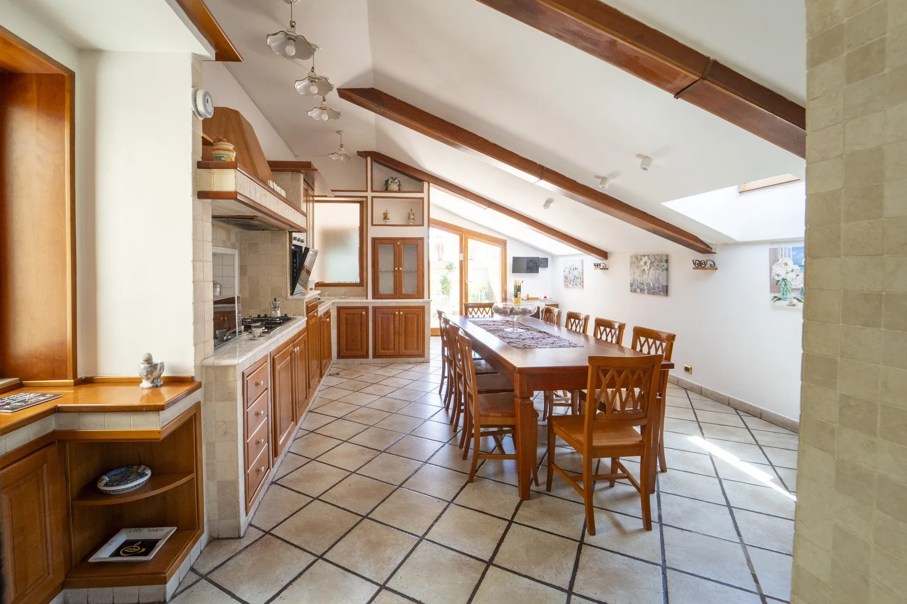 A bright open kitchen and dining area with wooden cabinetry and a long dining table.
