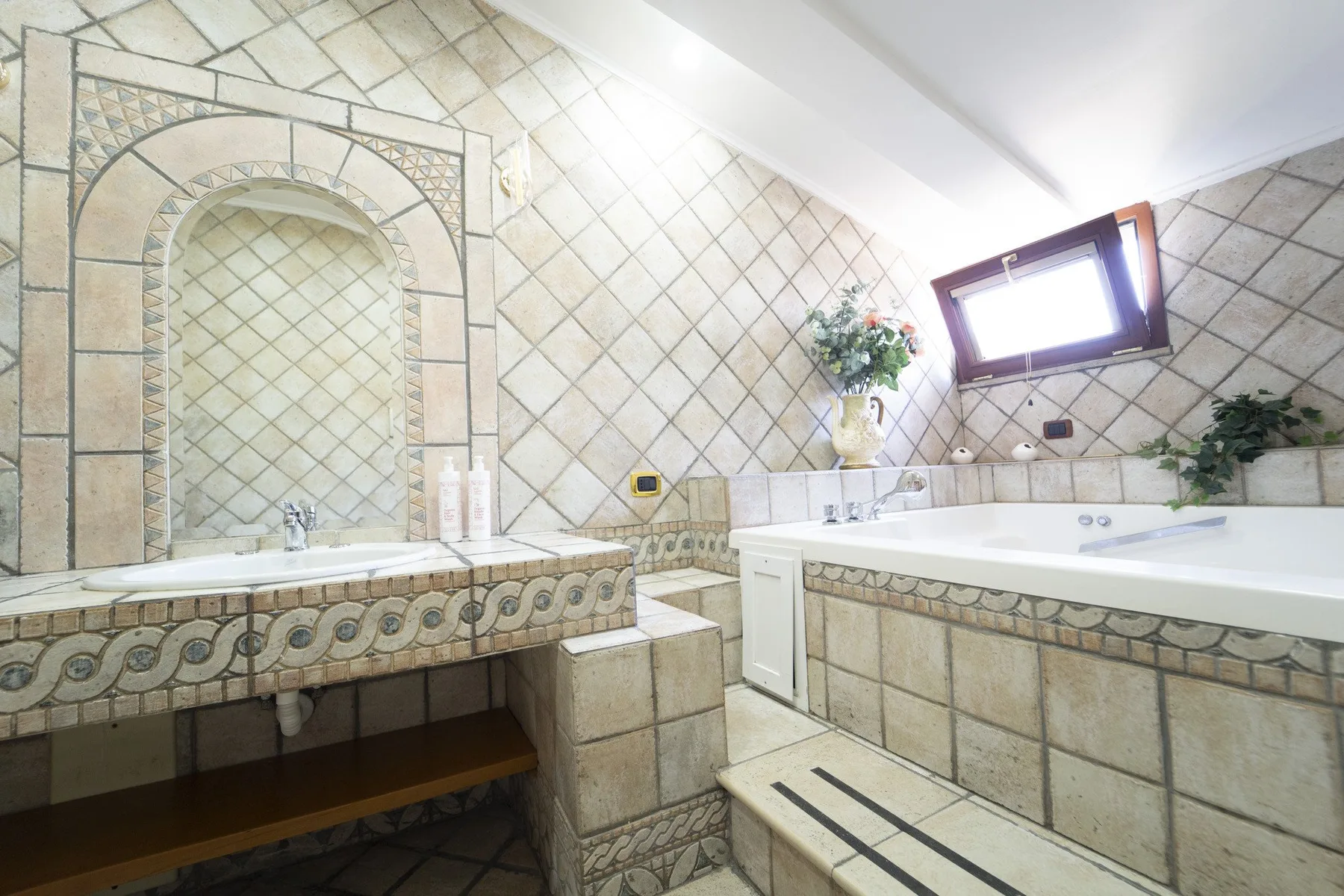 A tiled bathroom with a bathtub, a built-in basin, and a small window.