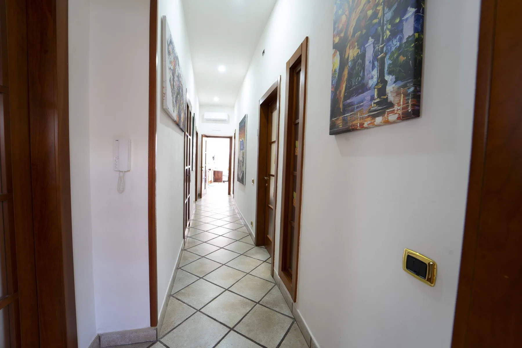A bright hallway with tiled flooring, framed artwork, and several doorways.